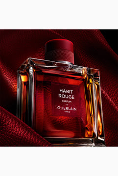 Bottle of Guerlain Habit Rouge perfume on a red background