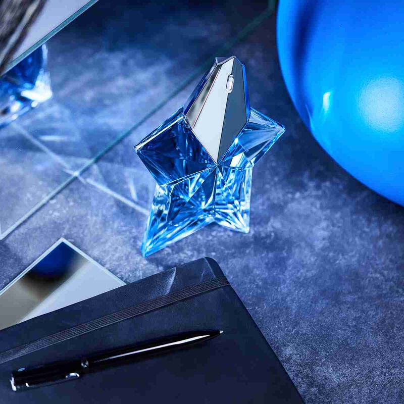 Blue star-shaped perfume bottle on a dark surface with a pen and notebook.