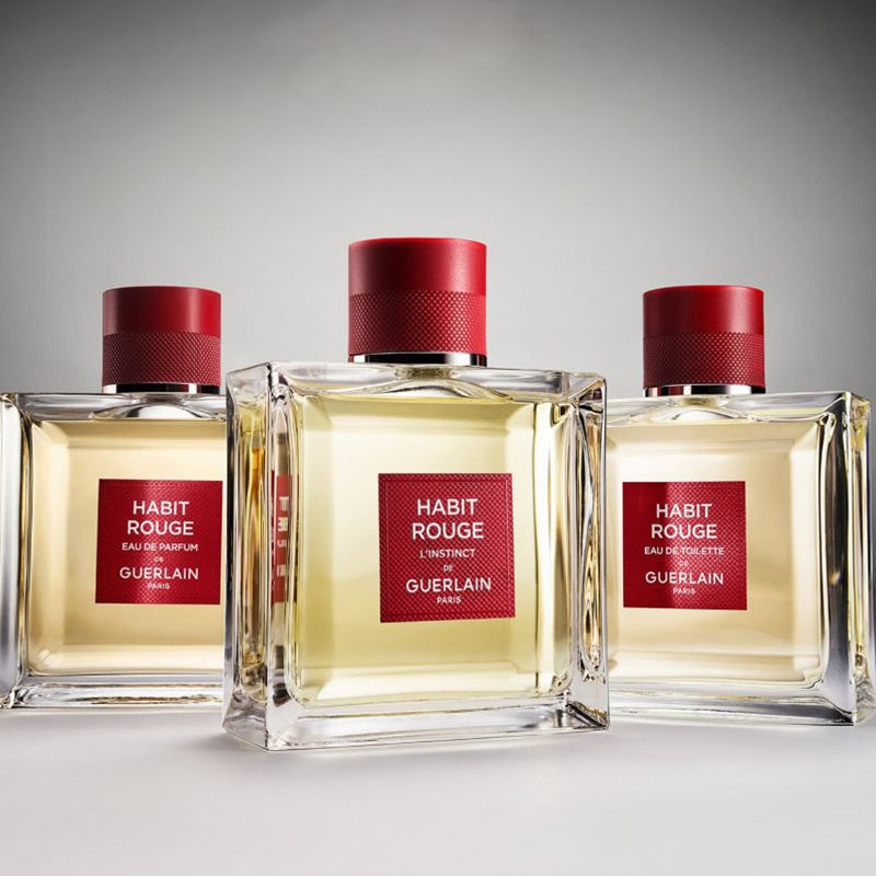 Three bottles of Habit Rouge perfume by Guerlain on a gray background