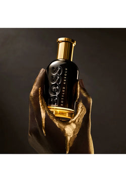 Bottle of Hugo Boss perfume held by a hand against a dark background