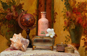 Decorative still life with a pink bottle, seashell, and globe against a floral wallpaper background.