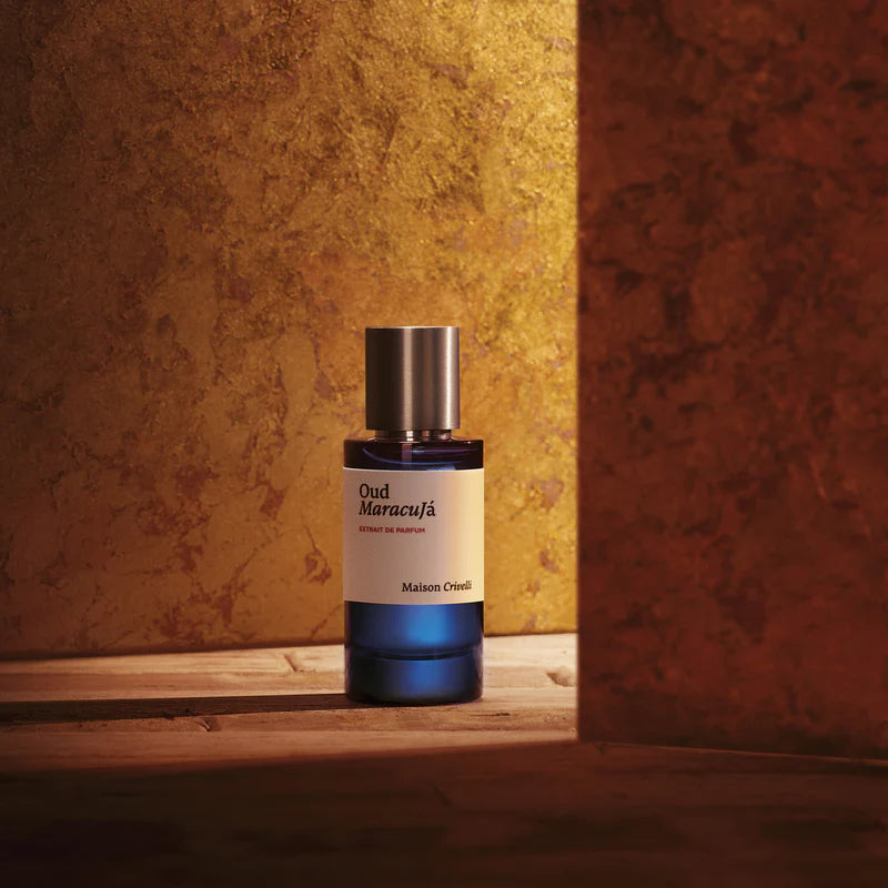 Perfume bottle labeled 'Oud Maracuja' on a wooden surface with a textured gold and red wall background