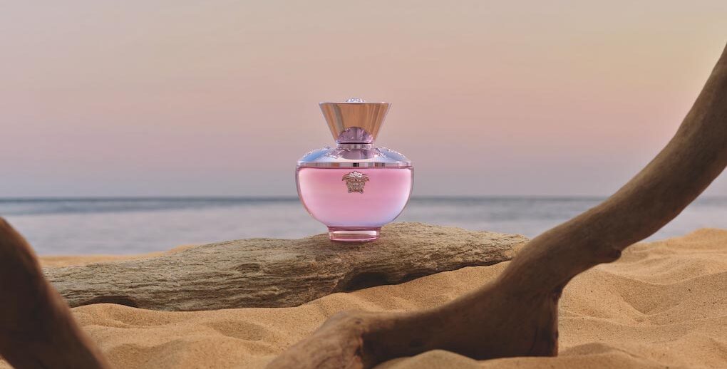 Pink perfume bottle on a log with a beach background
