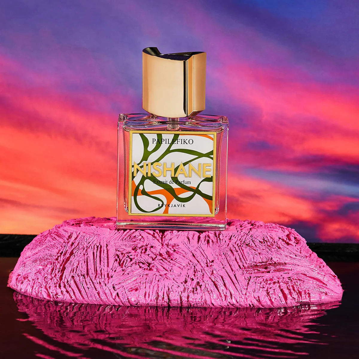 Perfume bottle with colorful label on a pink textured surface against a vibrant sunset sky