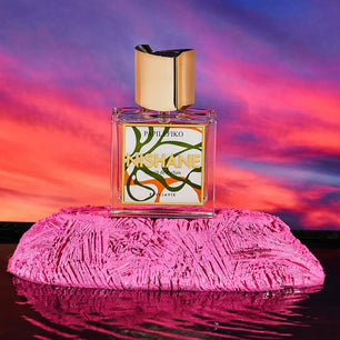Perfume bottle with colorful label on a pink textured surface against a vibrant sunset sky