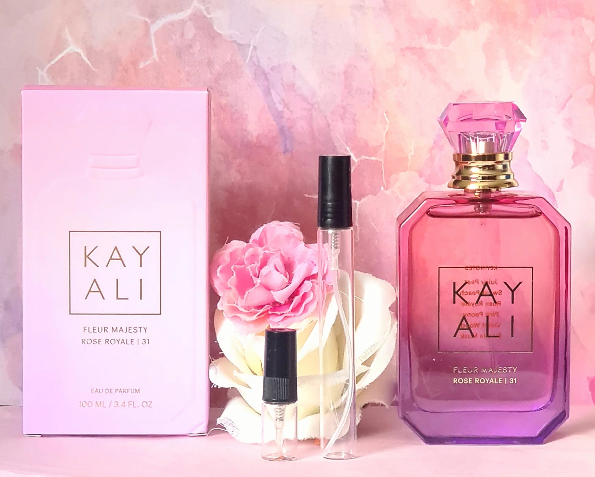 Kay Ali perfume set with bottle, box, and flowers on a pink marble background